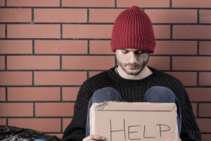 Homeless man with Help sign, wearing a red hat