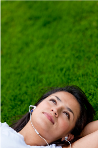 Listening to music is an activity mentioned in this month's blog. Shows a woman lying in grass with headset on.